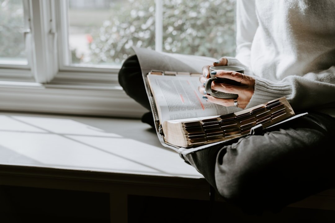 Person writing thoughtfully in a journal near a window