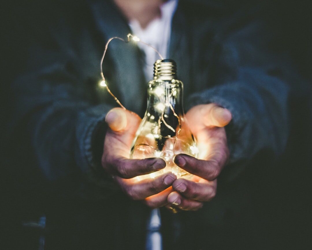 Hand holding a glowing light bulb against a dark background